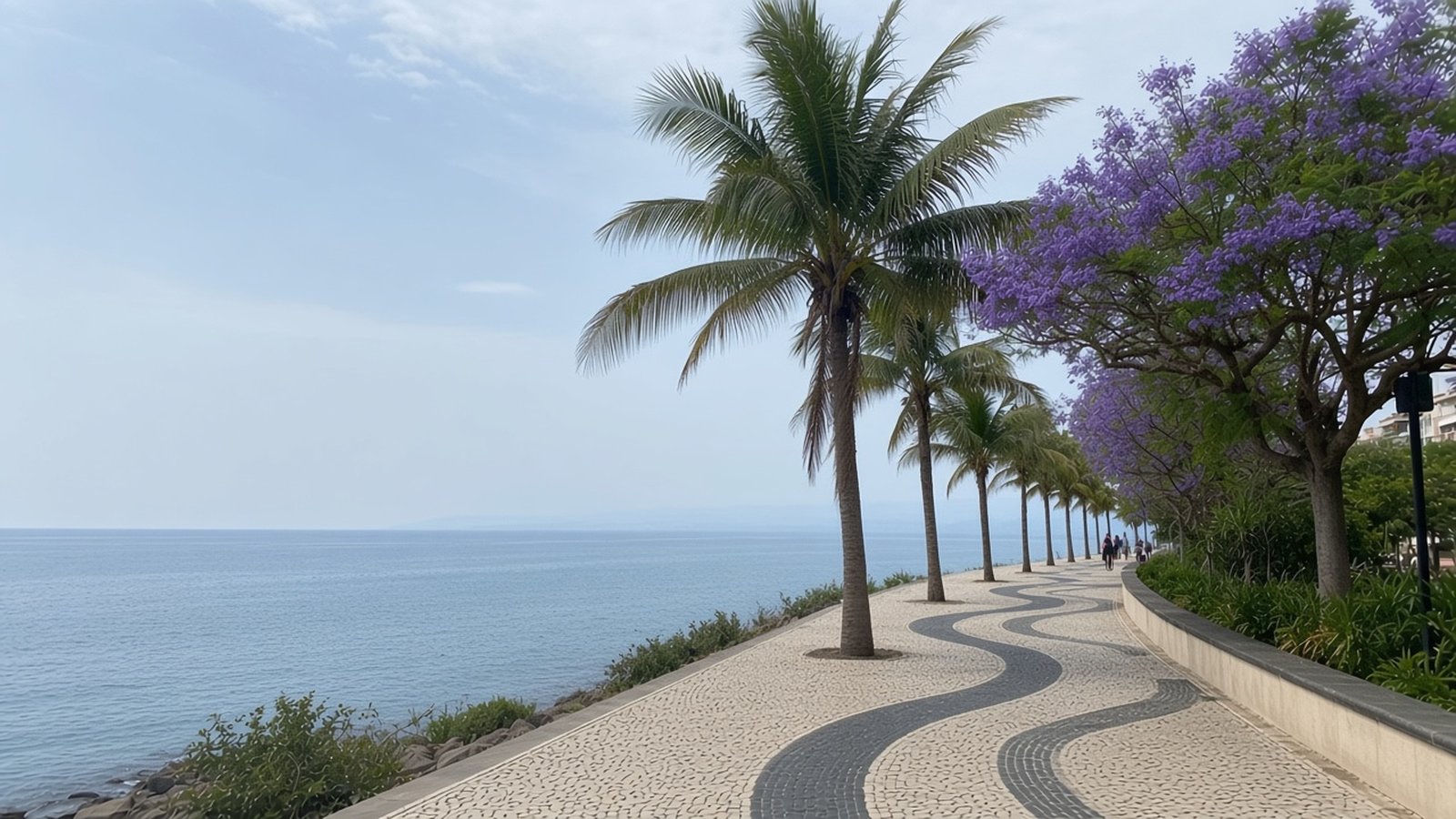 A palm-lined seafront promenade with patterned cobblestones and a flowering jacaranda by a calm sea