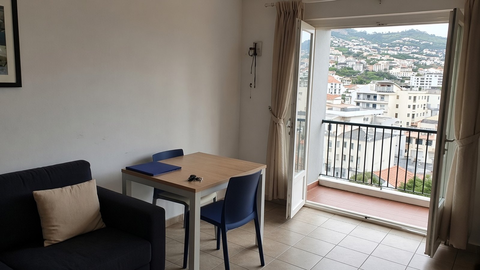 A simple furnished flat with keys on the table and an open balcony door facing Funchal's hillside
