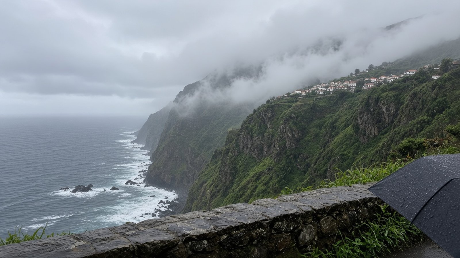 Low cloud and drizzle over steep green cliffs and a rough sea on Madeira's north coast