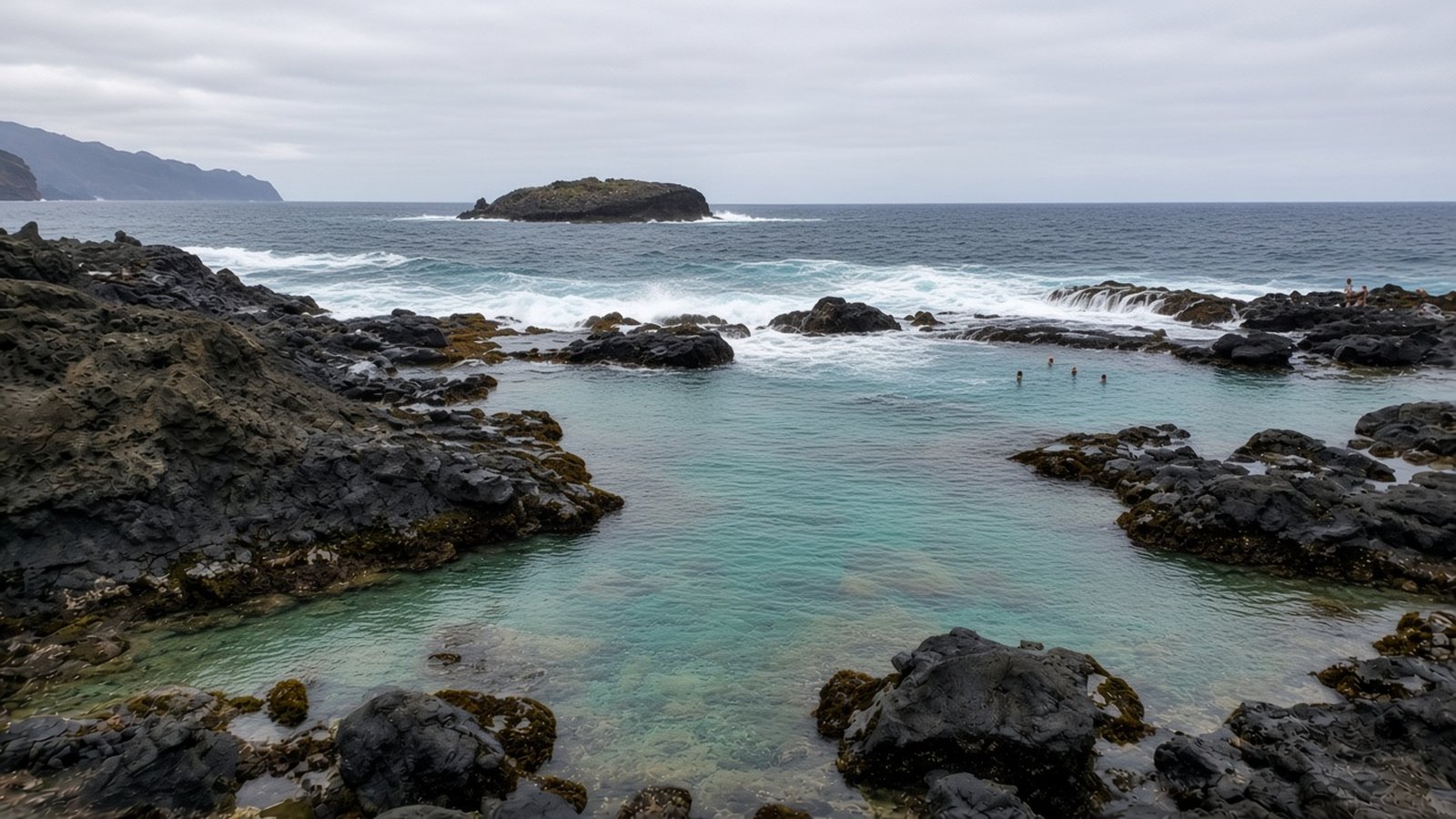 Clear turquoise seawater in black lava rock pools as Atlantic waves break on the outer rocks